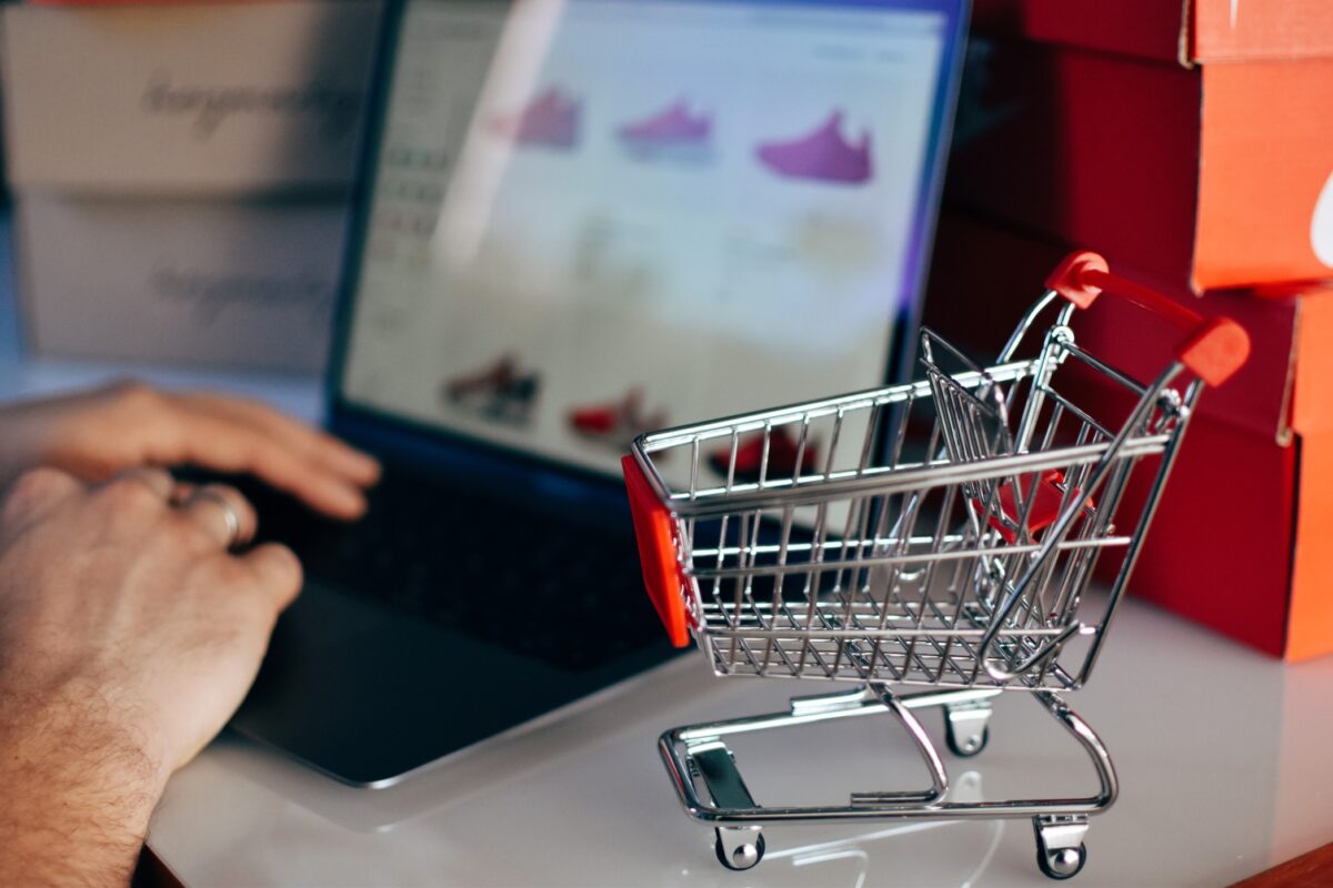 online shopping concept of miniature shopping cart and man using laptop for shopping online