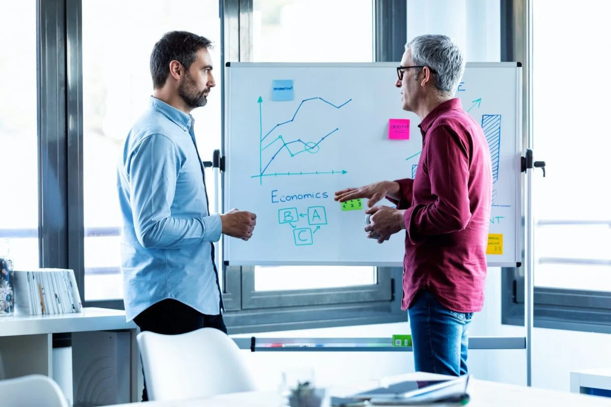 two businessmen discussing data on whiteboard e1619927450986 1