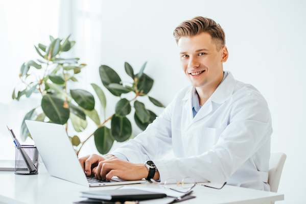 happy doctor looking at camera while using laptop