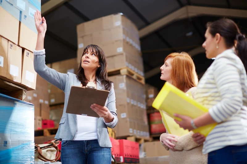 woman with clipboard in warehouse checking inventory with other employees