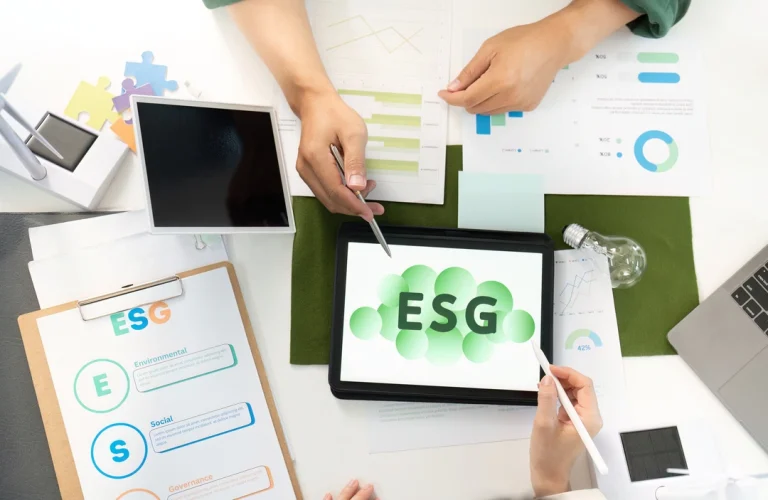 An overhead shot shows two sets of hands, one holding a stylus, reviewing what is ESG on tablets and printed graphs in an office setting.