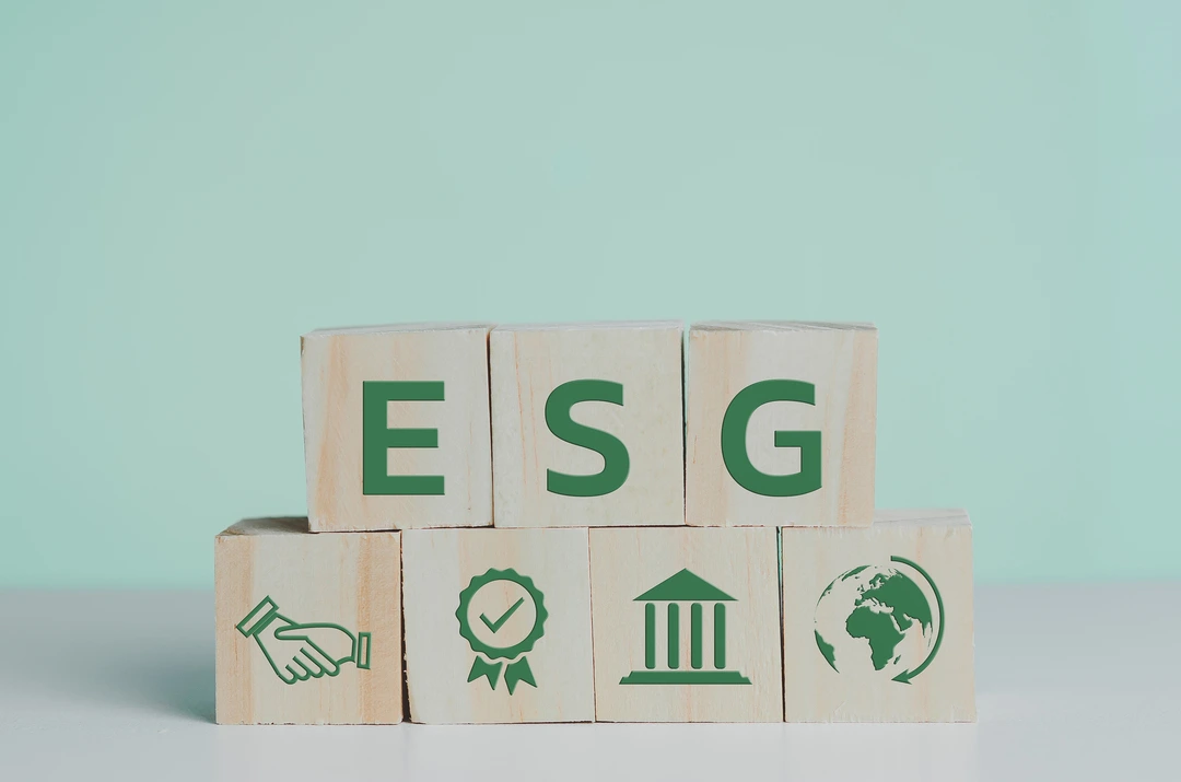 Wooden blocks spelling the letters ESG sit atop other blocks imprinted with sustainable concepts against a pale green background.
